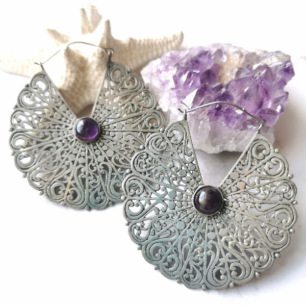 Decorative silver earrings with purple gemstones on a white background with amethyst crystal.