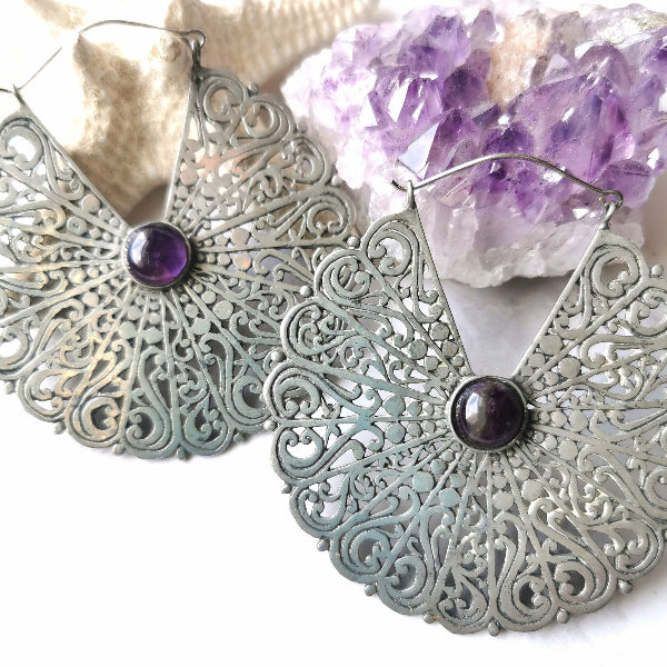 Silver filigree earrings with purple stones on a white background with crystals.