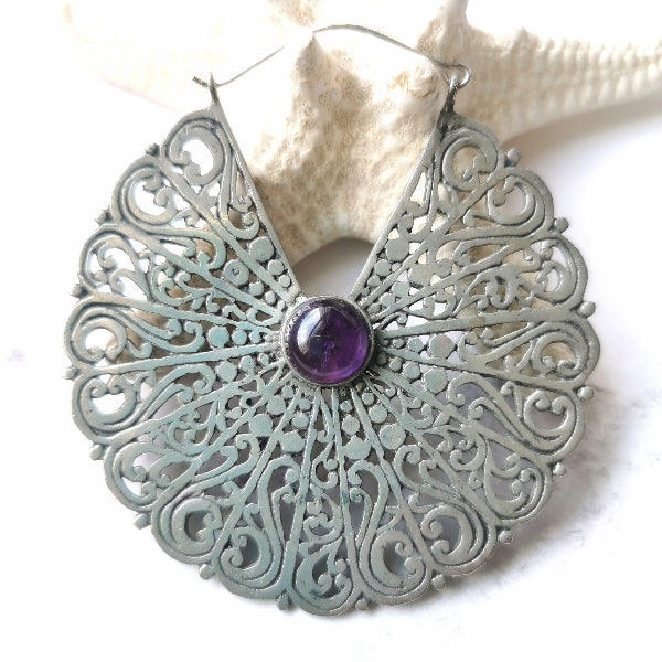 Decorative silver earring with a purple gemstone on a white background