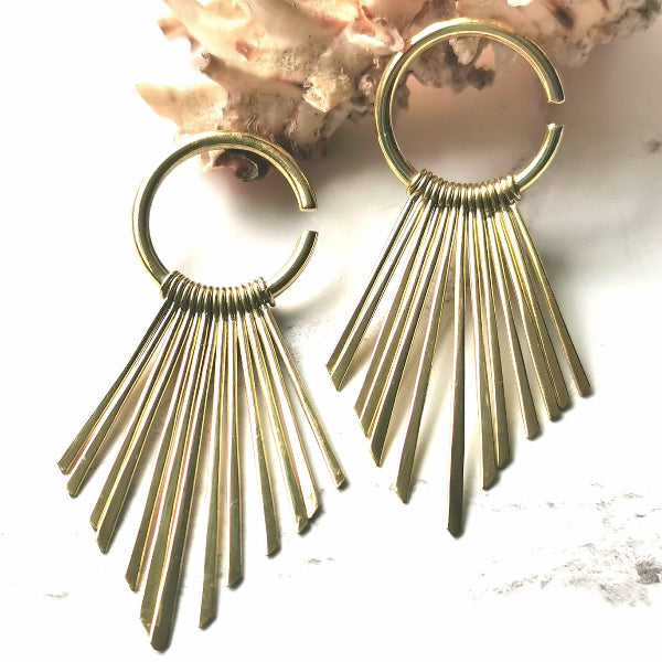 Gold fringe earrings on a textured white surface with a natural background