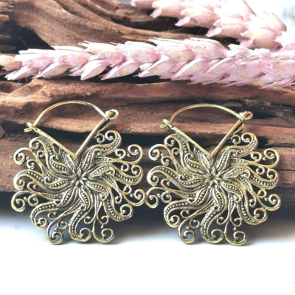 Gold floral earrings on a wooden surface with pink flowers.